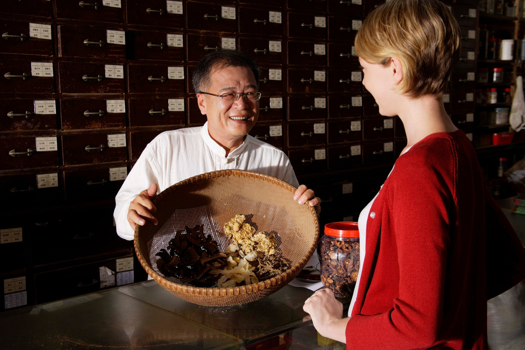 Chinese herbalist showing medicinal herbs to customer