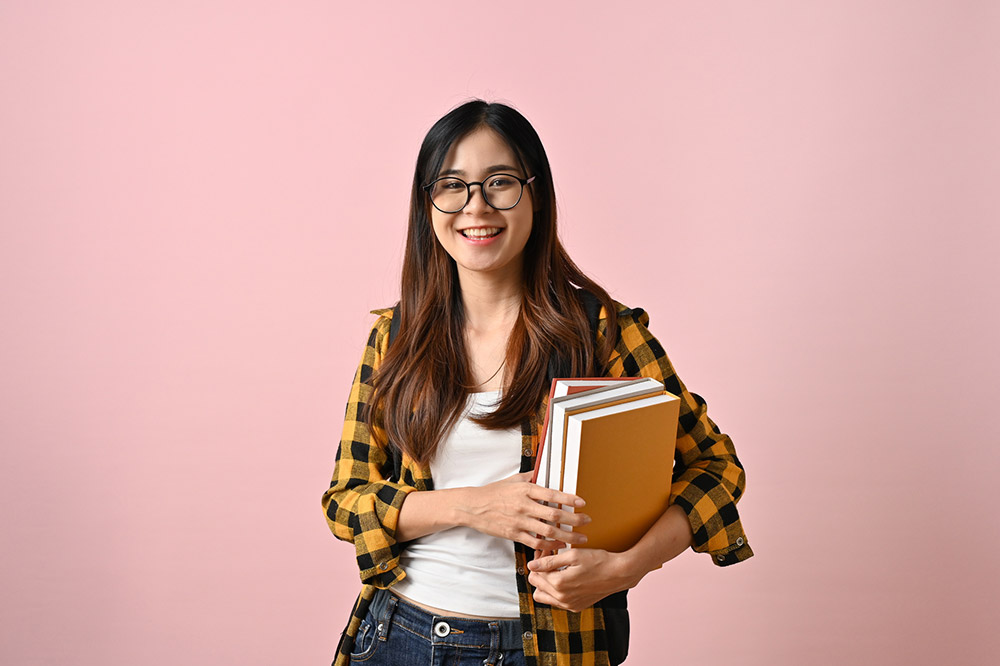 Wise Asian female college student holding books while standing a