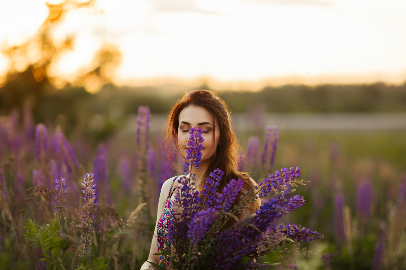Beautiful Young Woman Smelling Purple Flowers in the Field